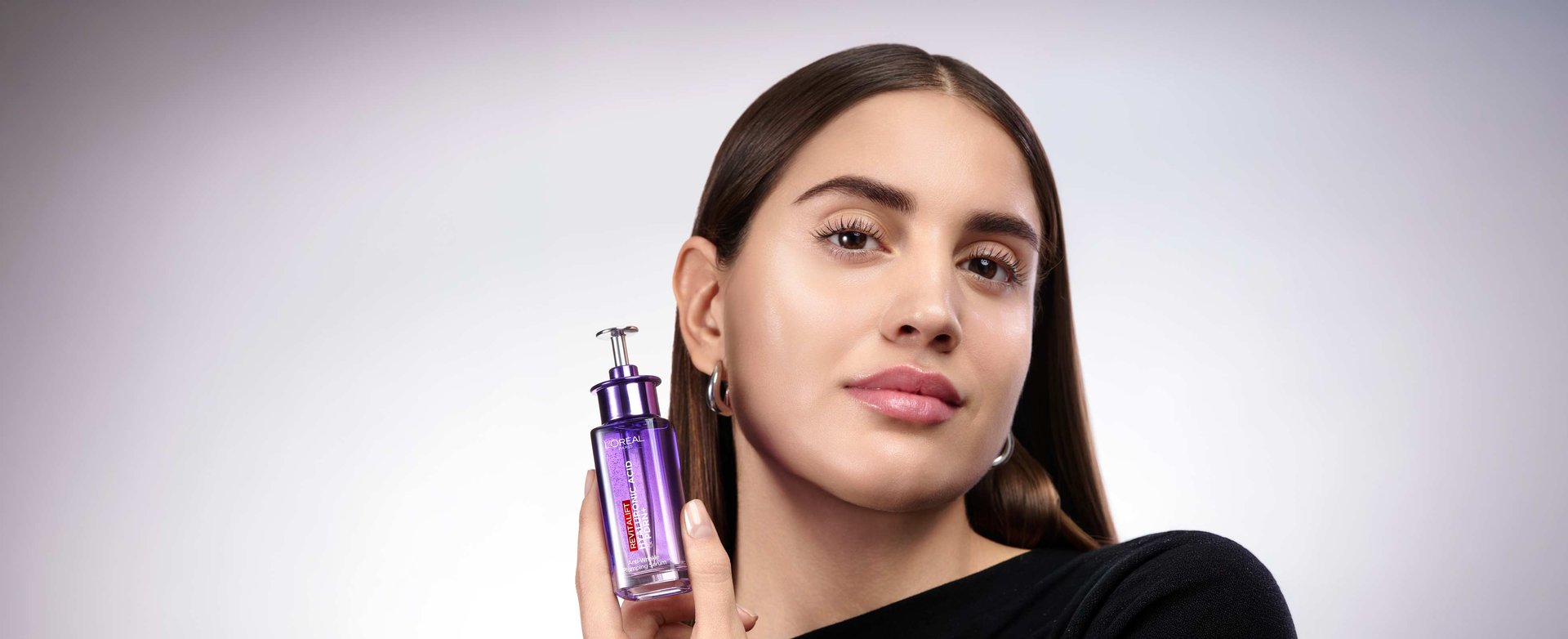 L'Oréal Paris Revitalift Filler Hyaluronic PDRN+ serum bottle beside a woman with radiant, glowing, mature skin.