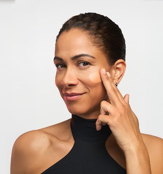 A woman with a radiant, youthful-looking complexion applying an anti-ageing facial serum, showcasing a structured daily L'Oréal Paris skincare routine.