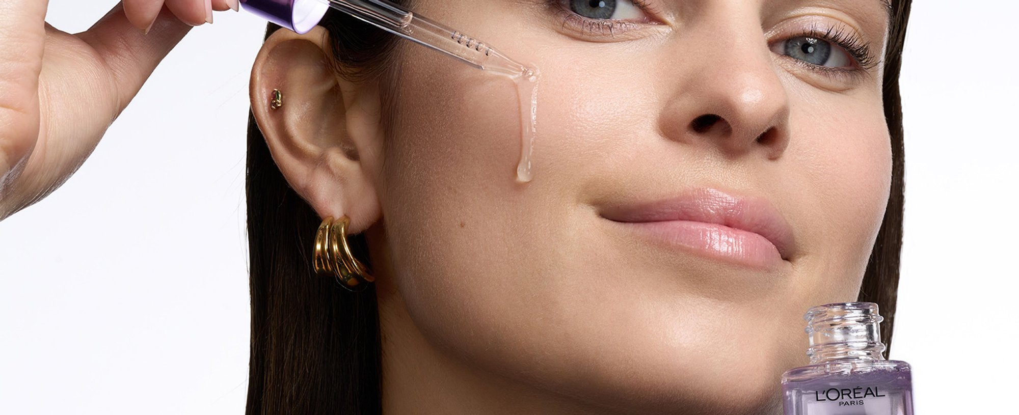 A woman applying L’Oréal Paris Revitalift serum to target fine lines, part of a scientifically validated daily anti-aging skincare routine.
