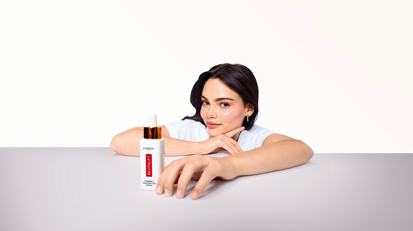 A model holding a bottle of L'Oréal Paris Revitalift Clinical Vitamin C Serum, demonstrating the daily antioxidant serum used to brighten skin and target early fine lines.