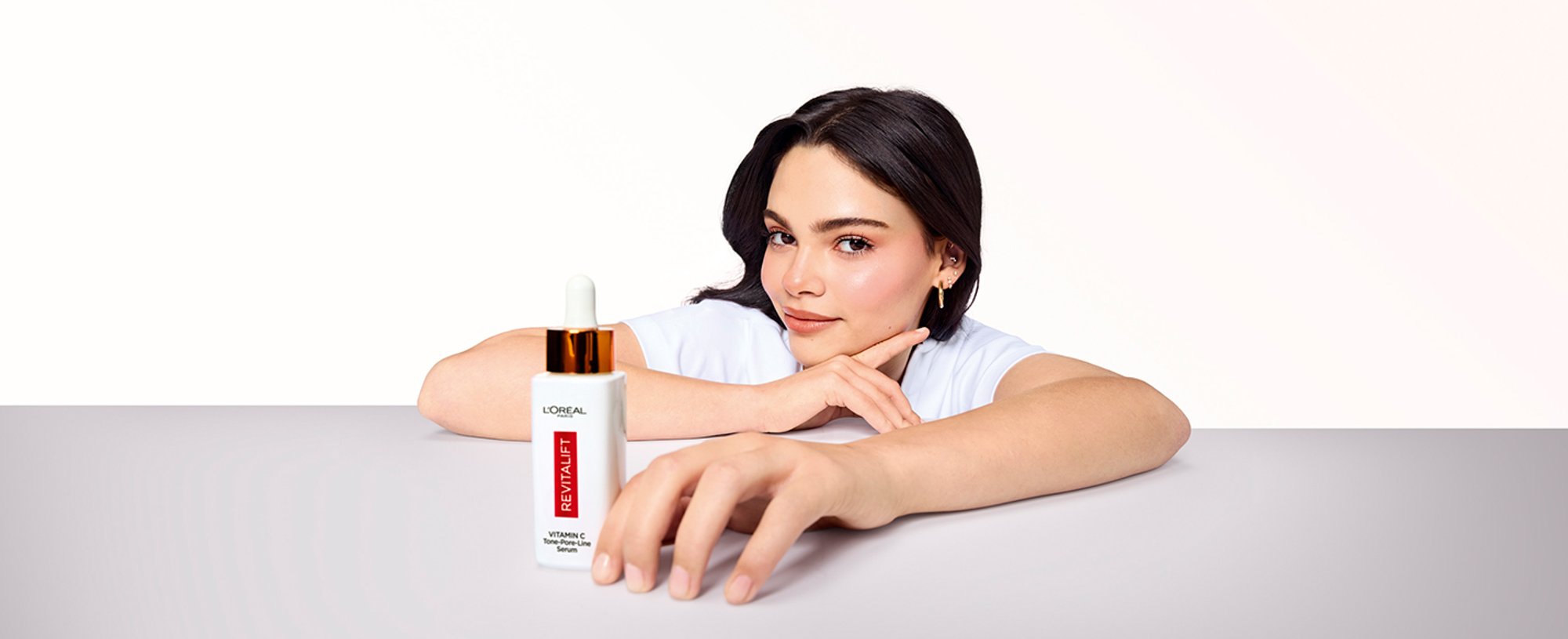 A model holding a bottle of L'Oréal Paris Revitalift Clinical Vitamin C Serum, demonstrating the daily antioxidant serum used to brighten skin and target early fine lines.