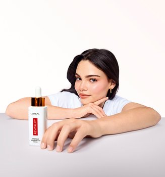 A model holding a bottle of L'Oréal Paris Revitalift Clinical Vitamin C Serum, demonstrating the daily antioxidant serum used to brighten skin and target early fine lines.